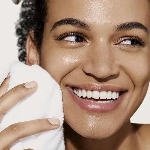 A woman smiling holding a towel to her face.